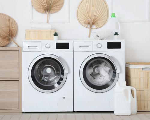 Interior of laundry room with washing machines, wooden cabinet and laundry basket